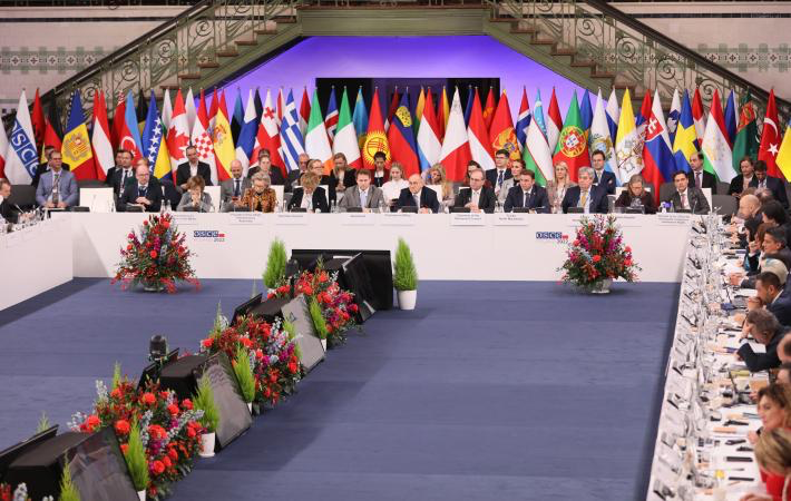 A group of people sitting on a stage with flags Description automatically generated with low confidence