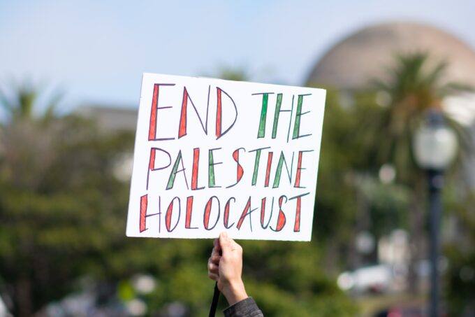 Image of a sign being held that reads End the Palestine Holocaust.