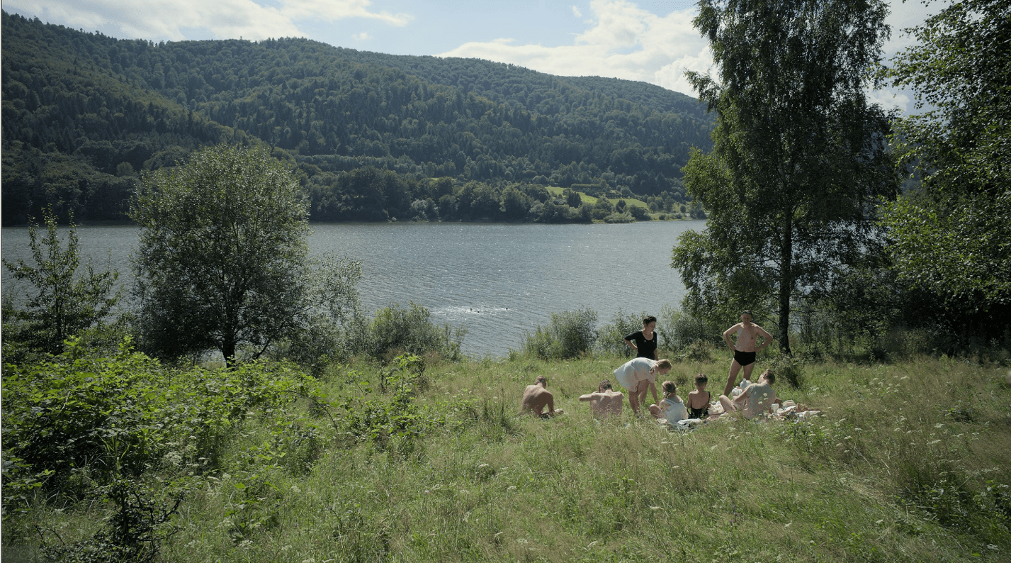 A group of people on a grassy hill by a lakeDescription automatically generated