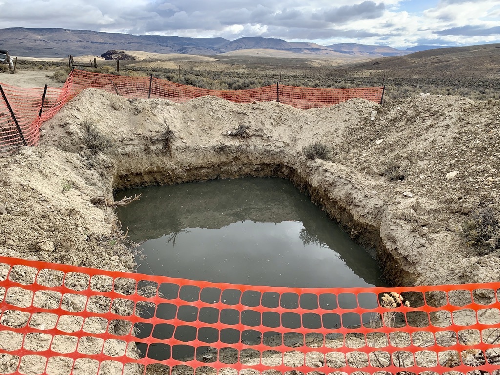 A hole in the dirt with a fence around itDescription automatically generated